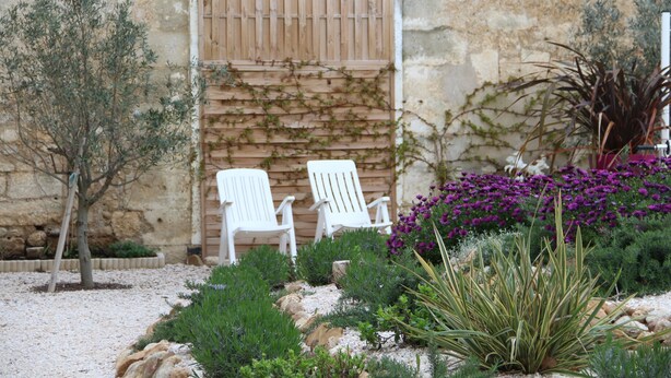 A garden with two white chairs, a stone wall, and various plants. - Country house with private heated pool 15mn from the sea (Vendres)