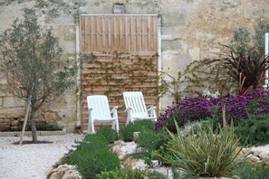 Ein Garten mit zwei weißen Stühlen, einer Steinmauer und verschiedenen Pflanzen.