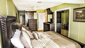 A bedroom with a large bed, a dresser, a mirror, and a ceiling fan.