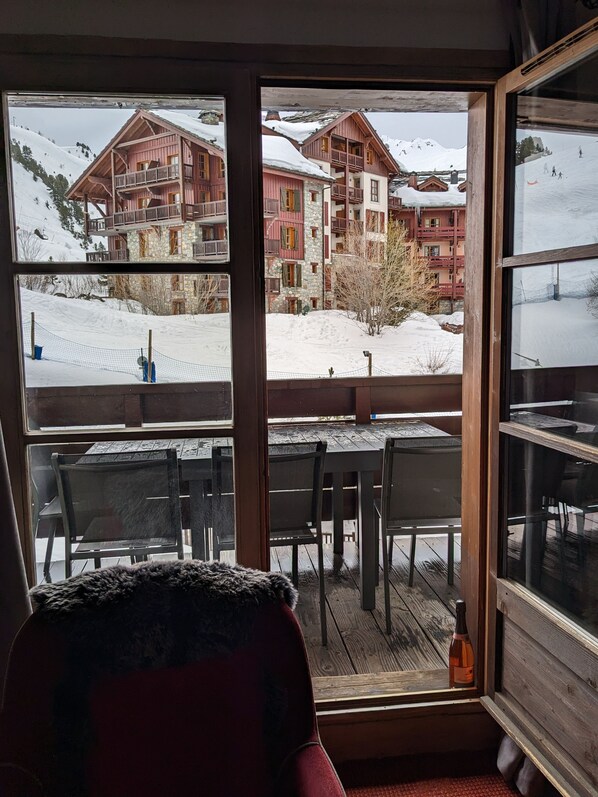 Une terrasse en bois, avec des chaises et une table, donnant sur un paysage enneigé parsemé de bâtiments.