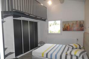 Un dormitorio con una cama, una ventana, un cuadro y una escalera.