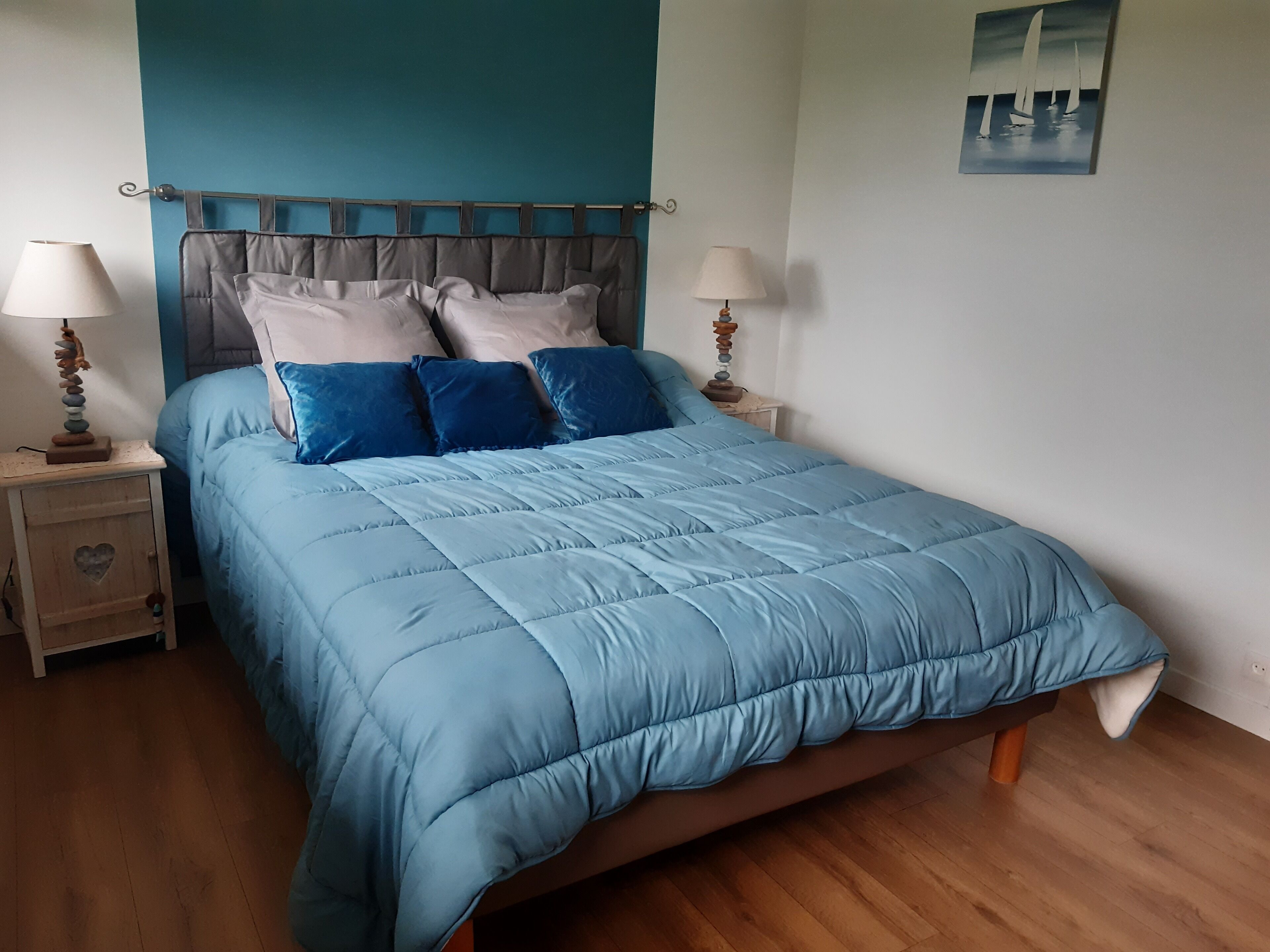 Un lit recouvert d’une couette bleue, deux tables de chevet avec des lampes et un tableau accroché au mur.