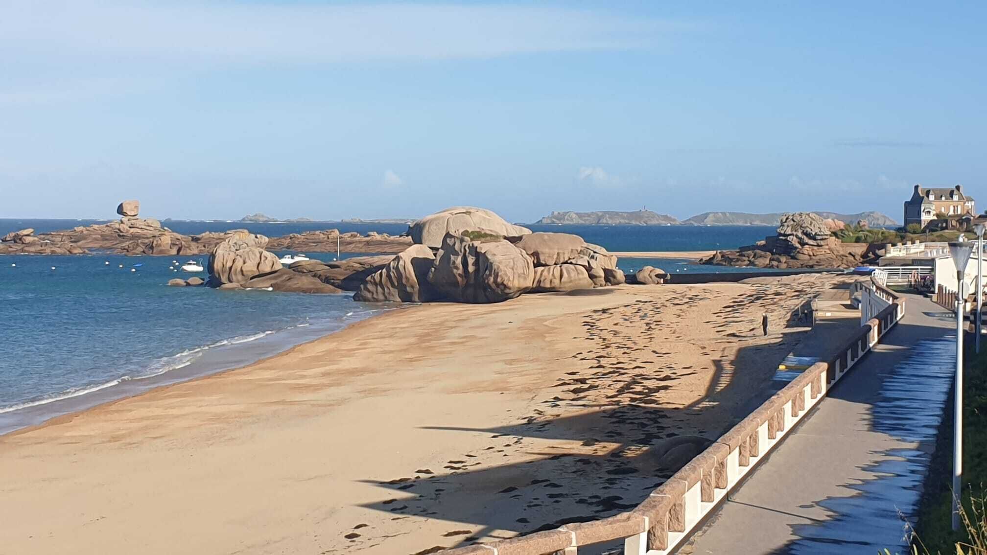 Une plage côtière bordée de gros rochers, avec une promenade pavée et un bâtiment doté d’un balcon donnant sur la mer.