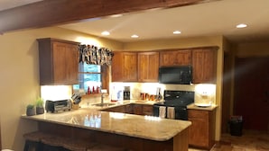 A kitchen with wooden cabinets, a granite countertop, a built-in island with bar stools, a microwave, and a stove.