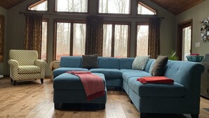 A living room with a blue sectional sofa, a patterned armchair, and a wooden ceiling.