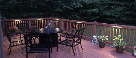 A wooden deck with a round table and chairs, surrounded by potted plants and a small frog statue.