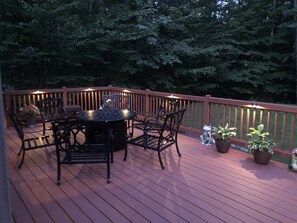 A wooden deck with a round table and chairs, surrounded by potted plants and a small frog statue.