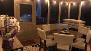 A covered patio area with a round table and chairs, string lights, and a view of the backyard.