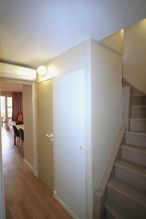 A hallway with a staircase, a door, and a dining area with chairs and a table.