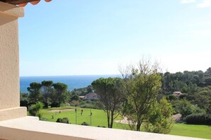 Un balcon offrant une vue sur un terrain de golf, des arbres et une côte lointaine.