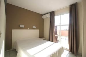 Une chambre d’hôtel avec un lit, une table de chevet, un climatiseur fixé au mur et une fenêtre avec des rideaux.
