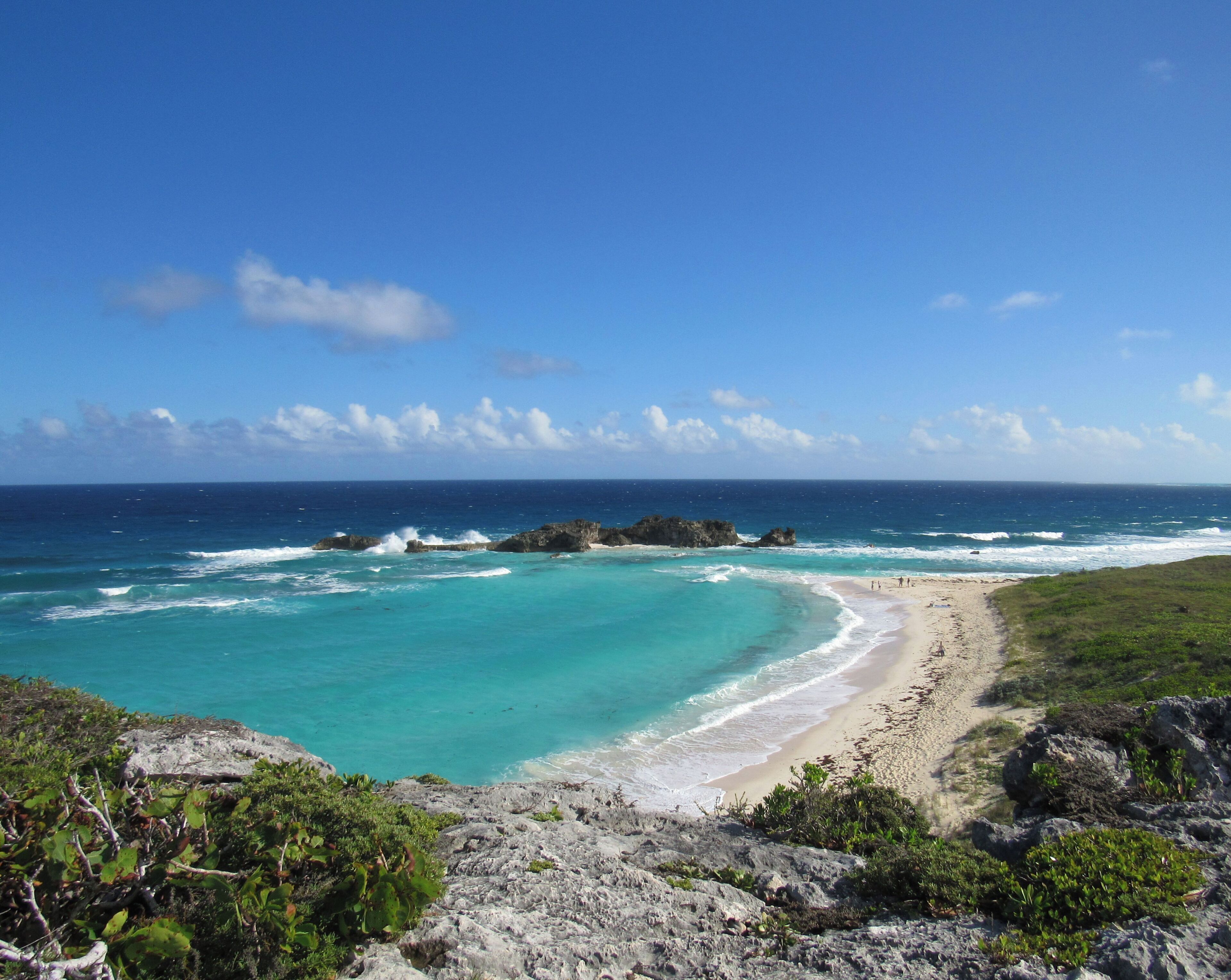 A coastal landscape with a sandy beach, rocky outcrops, and clear turquoise waters.
