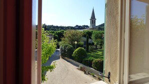 A view from a window overlooking a street with a church spire, greenery, and a clear sky.