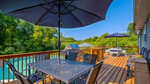 Une terrasse en bois avec une table et des chaises en métal, un barbecue et une piscine.