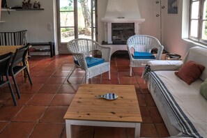 A cozy living room with a fireplace, wicker chairs, a sofa, and a tiled floor.