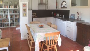Uma cozinha compacta com armários brancos, uma mesa de jantar com cadeiras e uma estante cheia de livros.