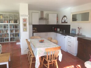 A compact kitchen with white cabinets, a dining table with chairs, and a bookshelf filled with books.