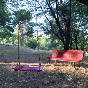 A red bench and a swing set in a park with trees and grass.