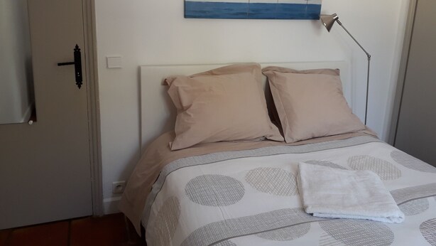Quarto com cama, almofadas bege, manta branca, pintura de criatura marinha e abajur.