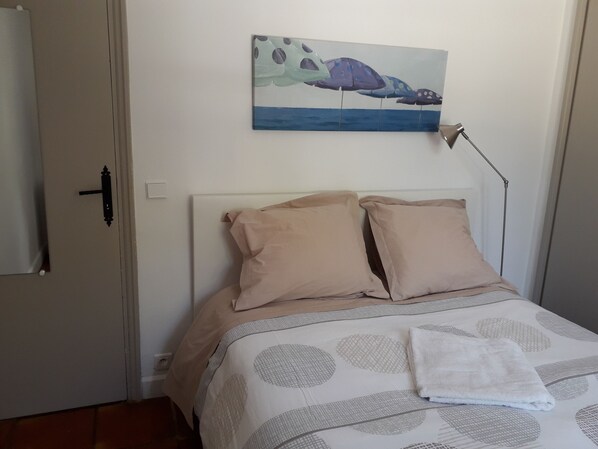 A bedroom with a bed, beige pillows, a white blanket, a painting of a sea creature, and a bedside lamp.