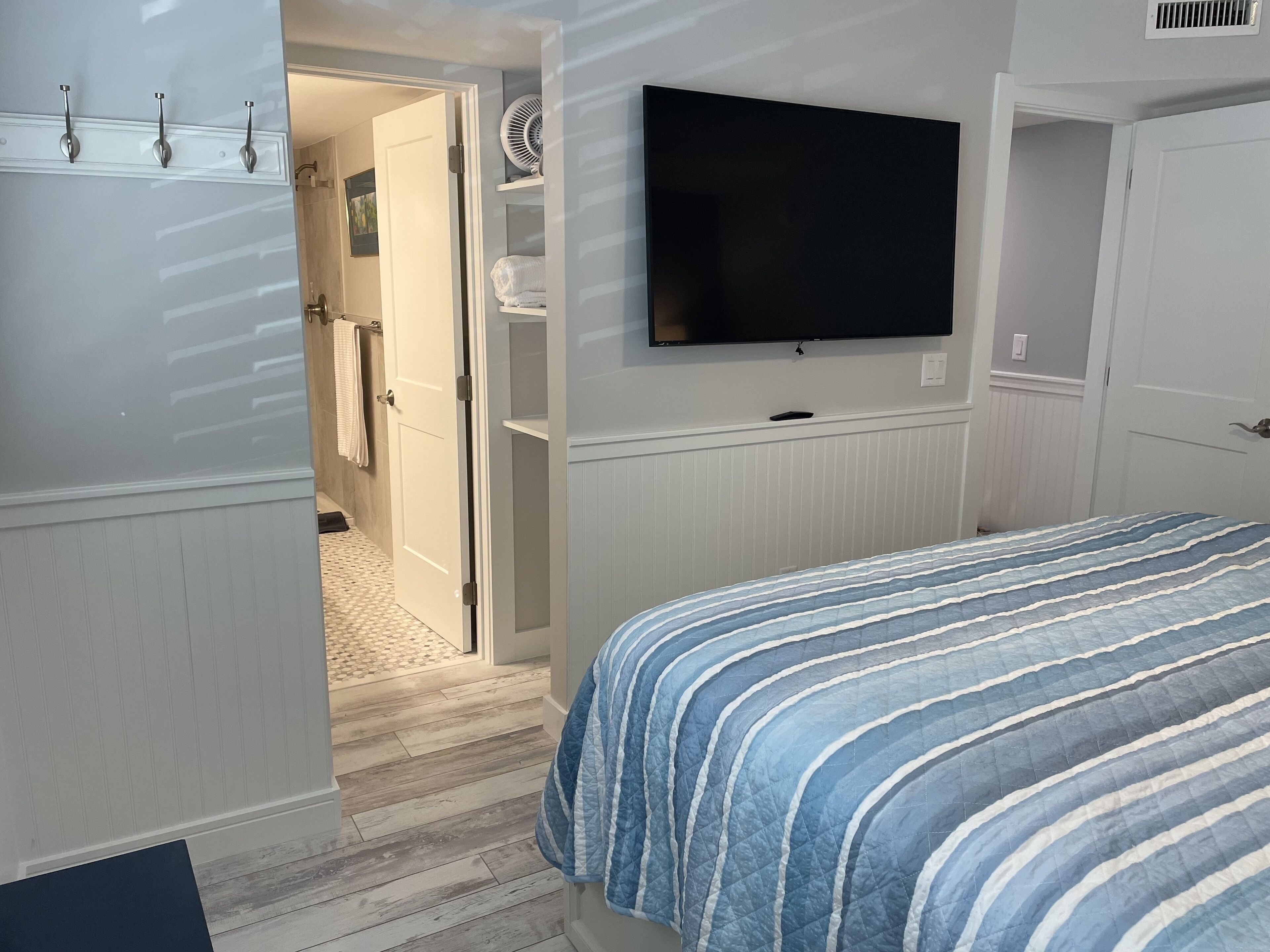 Ein Schlafzimmer mit Bett, einem an der Wand befestigten Fernseher, einer Tür zu einem Badezimmer und einem Flur.