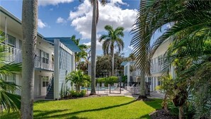 A courtyard with a swimming pool, palm trees, and a two-story building with balconies. - One block to beach and to dining. Best location in Naples !! (Naples)