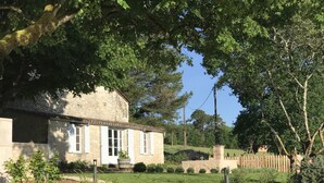 Ein Steinhaus mit weißen Fensterläden, umgeben von einem gepflegten Garten und einem Holzzaun.