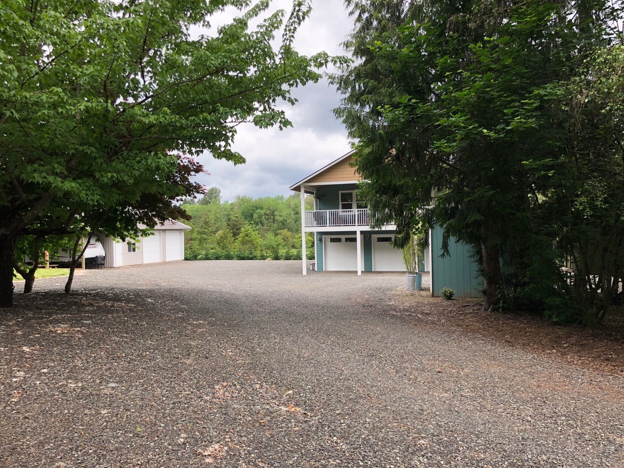 A two-story building with a balcony, surrounded by trees and a gravel driveway.