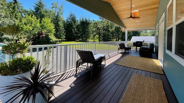 Una terraza techada con mobiliario exterior, un ventilador de techo y vistas a un paisaje verde.