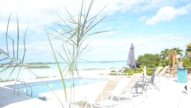 Ein Poolbereich mit Liegestühlen und Sonnenschirmen mit Blick auf das klare blaue Meer und entfernte Inseln.