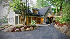 A two-story house with a covered porch, a stone pathway leading to the entrance, and a landscaped garden with rocks and plants. - New! Vermont modern farmhouse in Stowe Village (Stowe)
