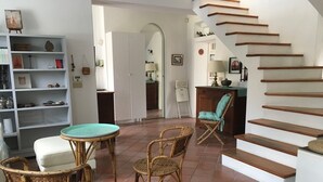 Een woonkamer met rieten meubilair, een ronde tafel en een trap.