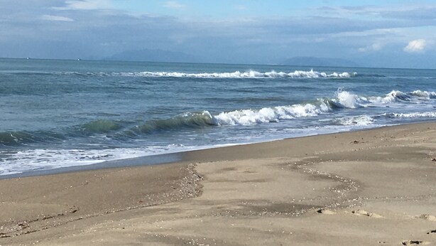 Een strand met golven, een heldere lucht en bergen in de verte.