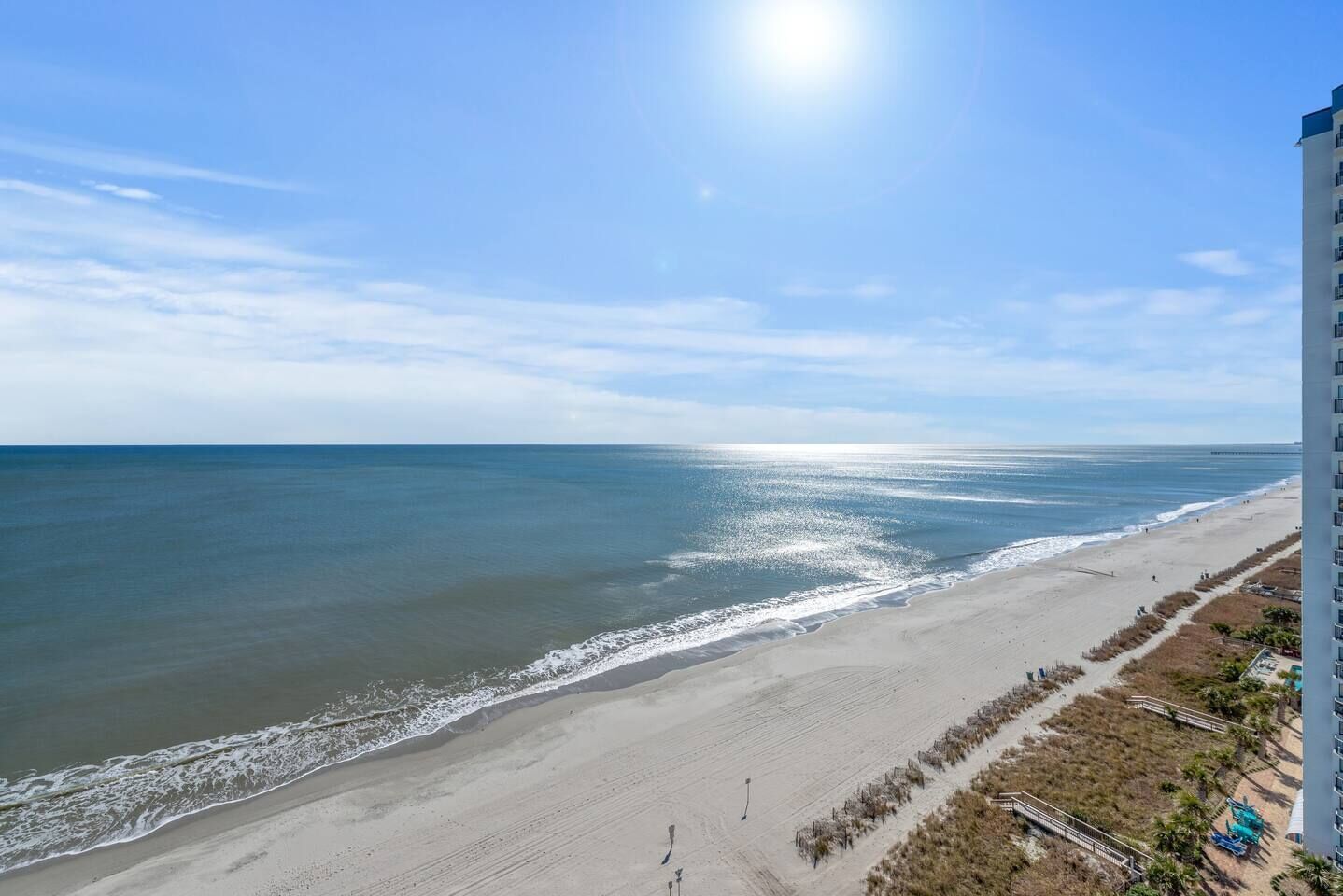 A beach view with a clear sky, a sandy shore, and a tall building on the right.
