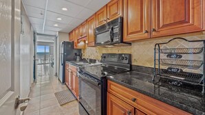 A kitchen with wooden cabinets, a black stove, and a microwave. - Impeccable Oceanfront Suite Top Floor (Myrtle Beach)