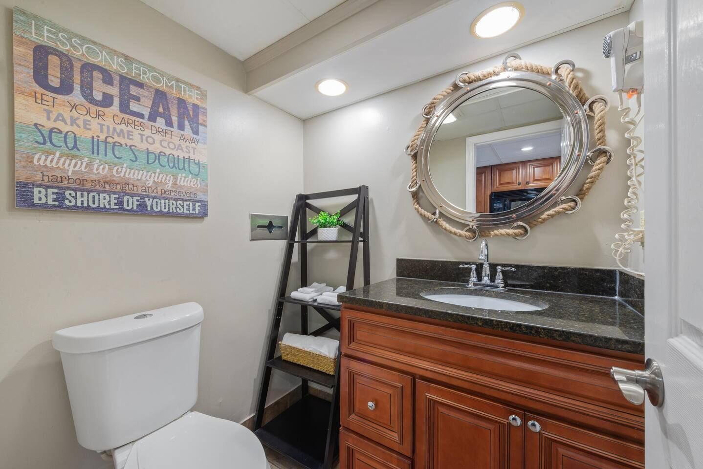 Un baño con inodoro, tocador con lavabo, espejo y una cita inspiradora en la pared.