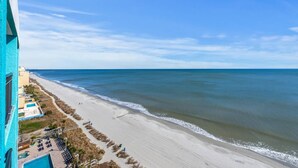 A beach view with a building on the left, a sandy beach, and the ocean. - Impeccable Oceanfront Suite Top Floor (Myrtle Beach)