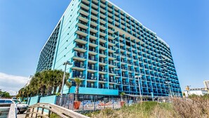 A high-rise hotel with a blue facade, multiple balconies, and a parking area in front. - Impeccable Oceanfront Suite Top Floor (Myrtle Beach)