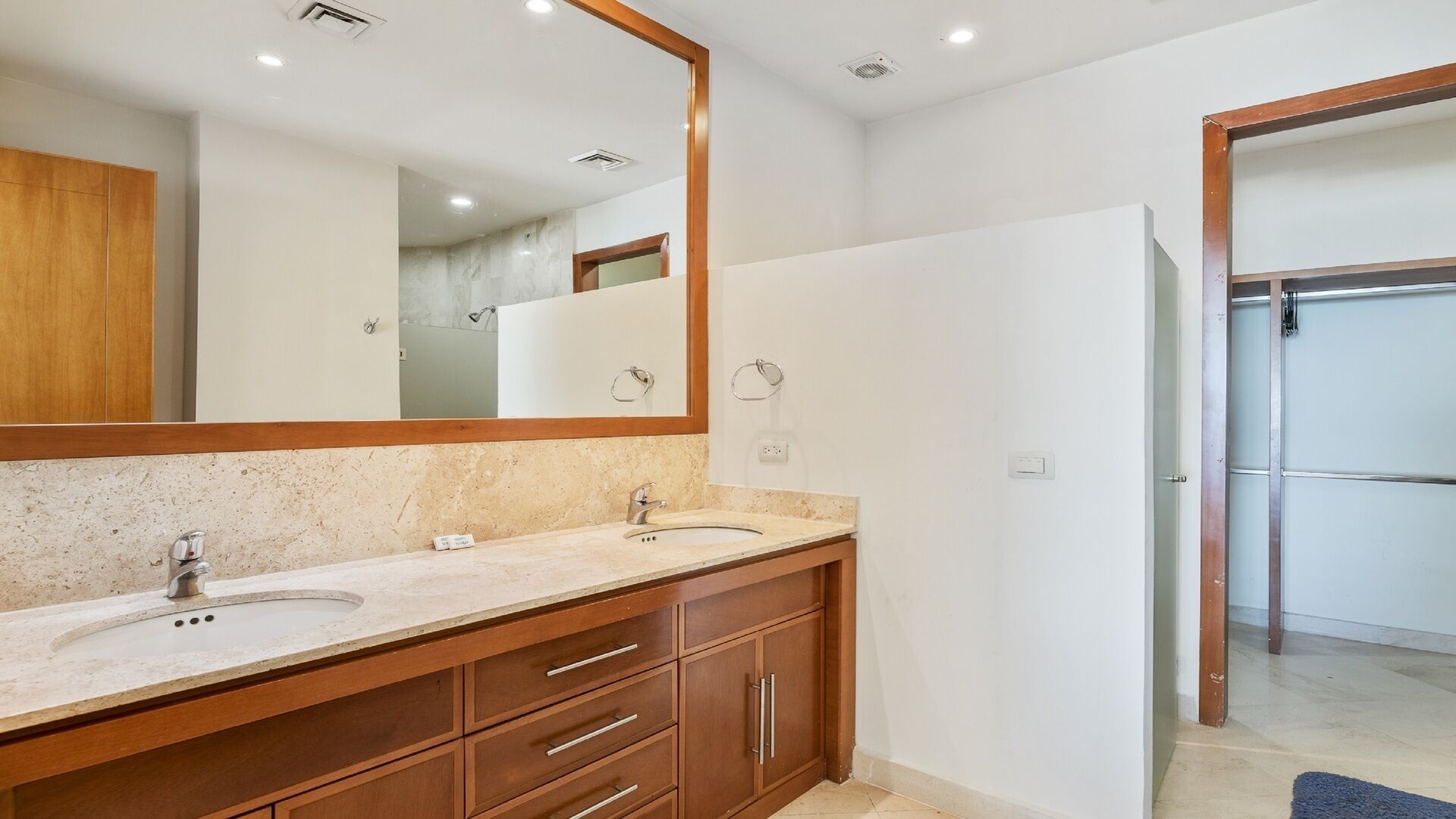 A modern bathroom with a double sink vanity, a large mirror, and a shower area visible through an open door.