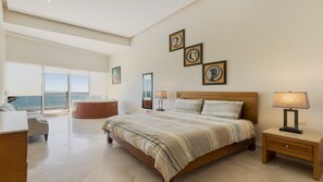 A spacious bedroom with a large bed, a sitting area with a view, and a hot tub.