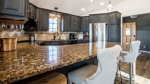 A modern kitchen with dark cabinetry, granite countertops, and a central island with bar stools.