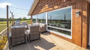 A wooden deck with wicker furniture and large windows overlooking a landscape.