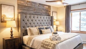 A bedroom with a tufted headboard, a large window with curtains, and a ceiling fan. - Spacious Lakefront Villa I 4 BD 3 Bath I Sleeps 11 I Ski I Golf I Bike (Biwabik)