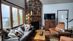 A living room with a stone fireplace, a sofa, a coffee table, a TV, and a chair. - Spacious Lakefront Villa I 4 BD 3 Bath I Sleeps 11 I Ski I Golf I Bike (Biwabik)