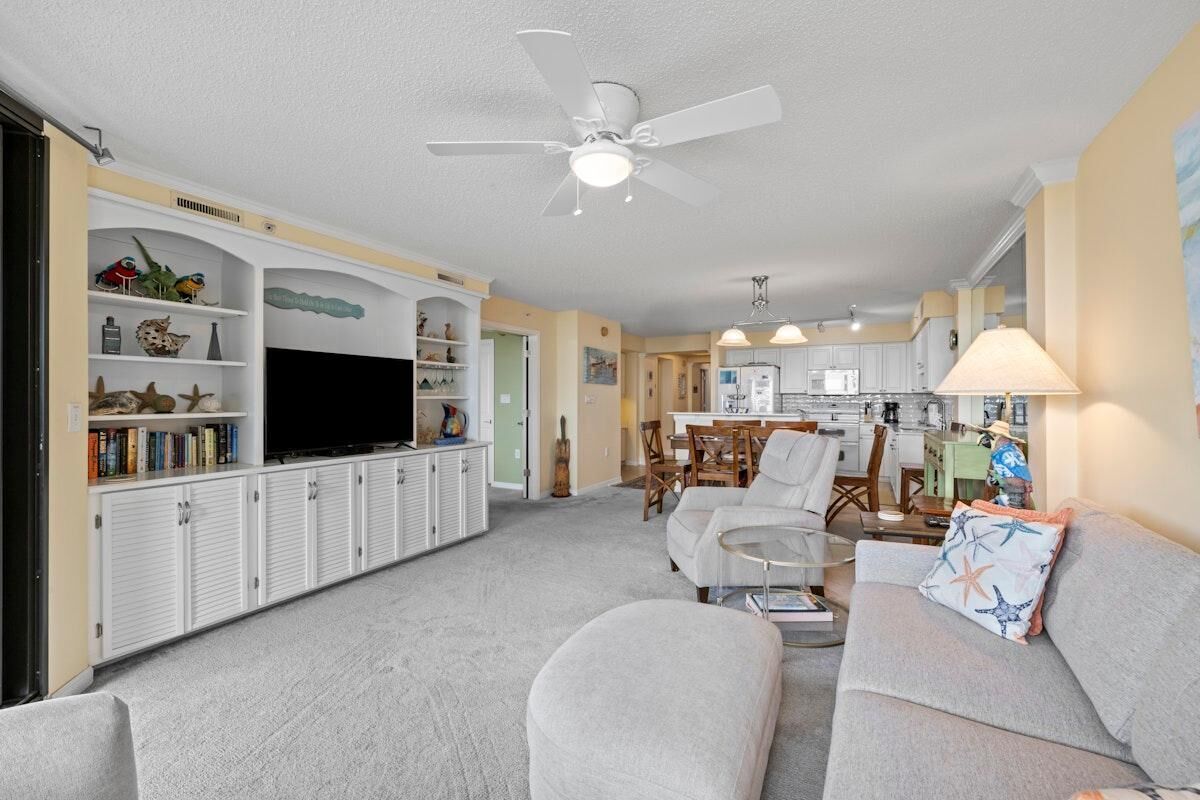 A living room with a sofa, TV, and entertainment unit, a dining area with chairs, and a kitchen in the background.