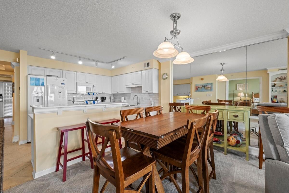A modern kitchen with white cabinets, a wooden dining table, and pendant lighting.