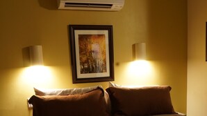 Une chambre d’hôtel avec un grand lit, deux lampes de chevet, un climatiseur et un tableau encadré au mur.