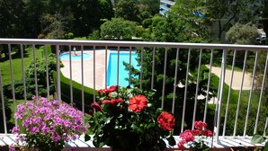 A balcony with potted flowers, a view of a swimming pool, and surrounding greenery. -  Antibes nice 3 rooms, clear and bright, beautiful sea view and swimming pool (Antibes)