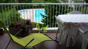A balcony with a view of a swimming pool, a table with a floral tablecloth, and a chair. -  Antibes nice 3 rooms, clear and bright, beautiful sea view and swimming pool (Antibes)