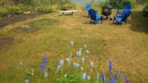 Un espace extérieur verdoyant avec trois chaises bleues, un banc et une lanterne.